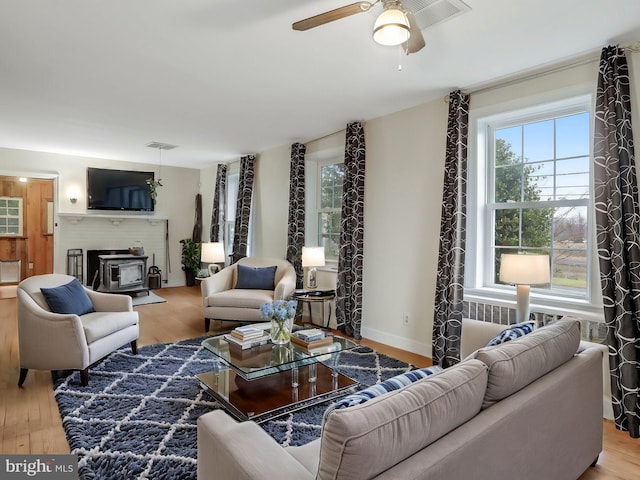 living area featuring visible vents, wood finished floors, a wood stove, and a ceiling fan