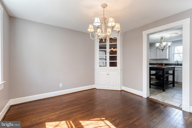 unfurnished dining area featuring baseboards, dark wood-type flooring, and a notable chandelier