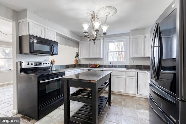 kitchen with an inviting chandelier, black appliances, white cabinets, and a healthy amount of sunlight