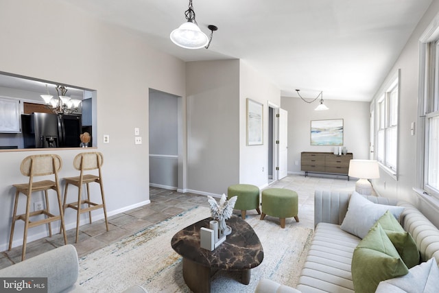 living room featuring baseboards, lofted ceiling, an inviting chandelier, and stone finish floor