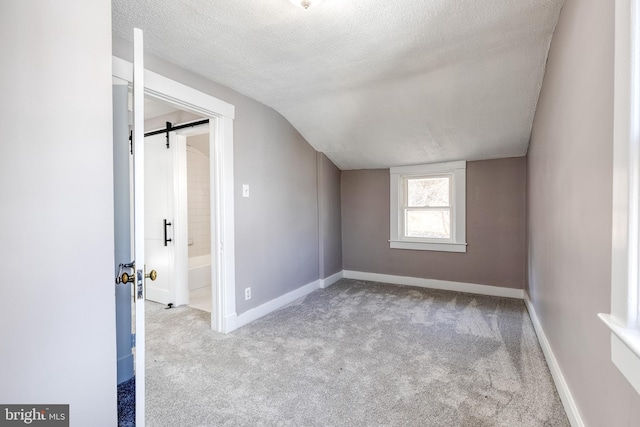 bonus room featuring baseboards, carpet, a barn door, vaulted ceiling, and a textured ceiling