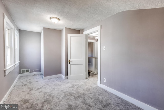 unfurnished room with visible vents, a textured ceiling, baseboards, and carpet