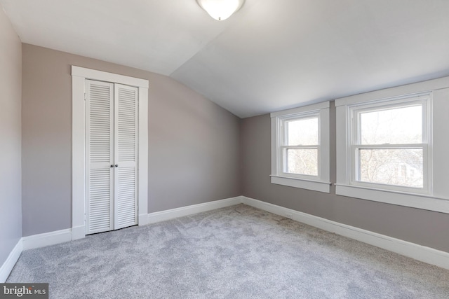 unfurnished bedroom featuring lofted ceiling, carpet flooring, baseboards, and a closet