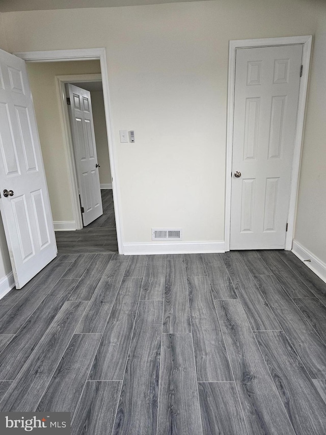 unfurnished bedroom with dark wood-style flooring, visible vents, and baseboards