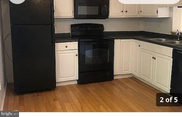 kitchen with black appliances, dark countertops, a sink, and light wood-style flooring