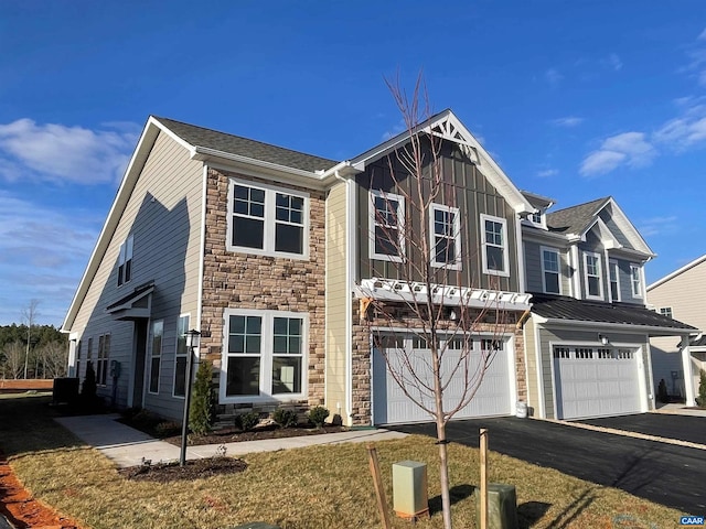 view of front facade with driveway, stone siding, an attached garage, a front lawn, and board and batten siding