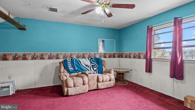 living area with ceiling fan, carpet flooring, visible vents, wainscoting, and a wall mounted air conditioner