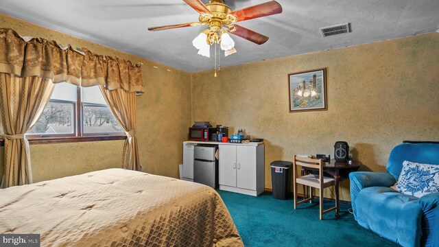 bedroom featuring freestanding refrigerator, visible vents, dark carpet, and ceiling fan