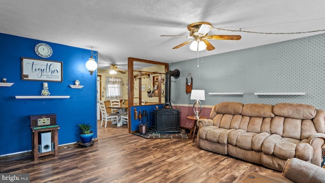 living area featuring a ceiling fan, wood finished floors, a wood stove, and wallpapered walls