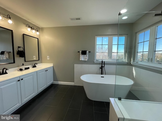 bathroom with a sink, visible vents, tile walls, a freestanding bath, and double vanity