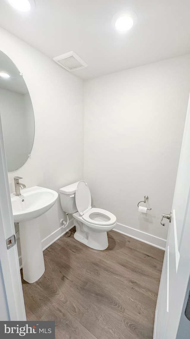 half bathroom with baseboards, visible vents, toilet, and wood finished floors