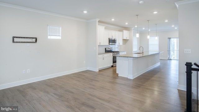 kitchen with a center island with sink, white cabinets, appliances with stainless steel finishes, wood finished floors, and crown molding