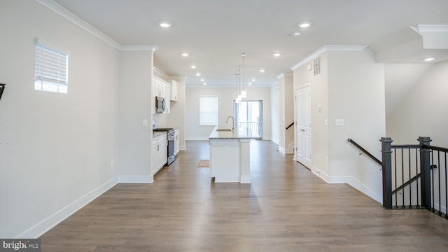 interior space featuring stainless steel appliances, a kitchen island with sink, white cabinets, a sink, and wood finished floors