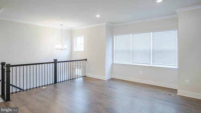 empty room with visible vents, a chandelier, wood finished floors, and ornamental molding