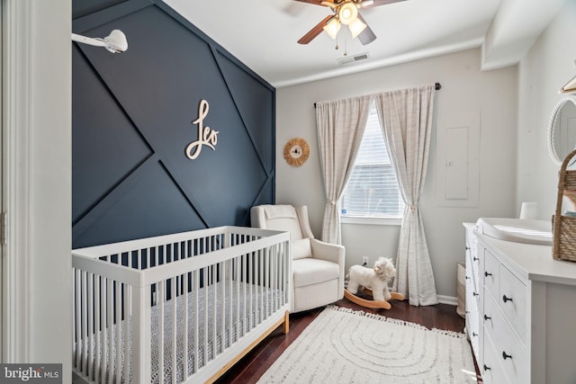 bedroom featuring visible vents, a crib, baseboards, dark wood-style floors, and a ceiling fan