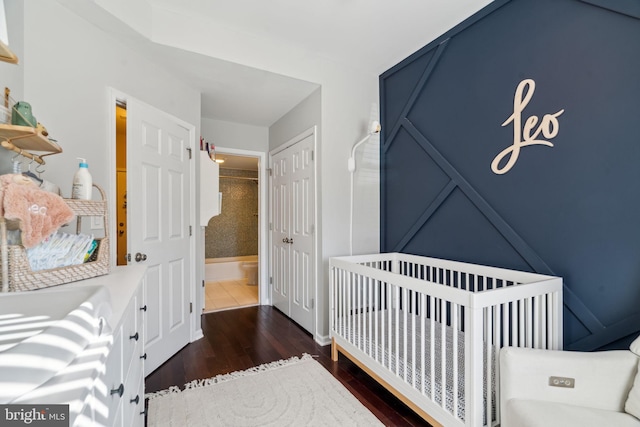 bedroom with a nursery area, a closet, and dark wood-type flooring