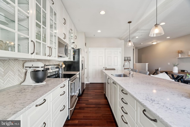 kitchen with tasteful backsplash, light stone countertops, appliances with stainless steel finishes, dark wood-style floors, and a sink