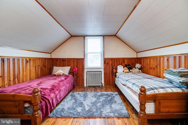 bedroom with lofted ceiling, radiator heating unit, wooden walls, and wood finished floors