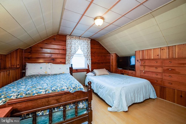 bedroom featuring vaulted ceiling, wood walls, and light wood-style flooring