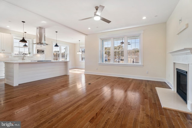 unfurnished living room featuring dark wood-style floors, recessed lighting, a fireplace with flush hearth, a ceiling fan, and baseboards