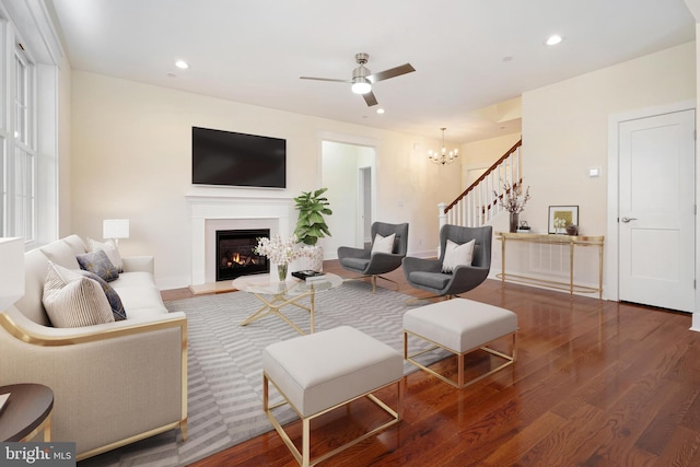 living room featuring a warm lit fireplace, stairway, dark wood finished floors, and recessed lighting