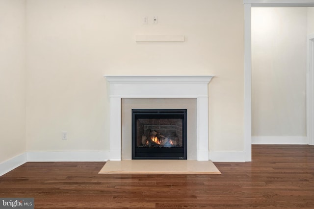 interior details featuring a warm lit fireplace, baseboards, and wood finished floors