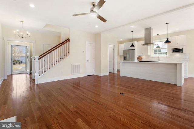 unfurnished living room with dark wood finished floors, visible vents, stairway, baseboards, and ceiling fan with notable chandelier