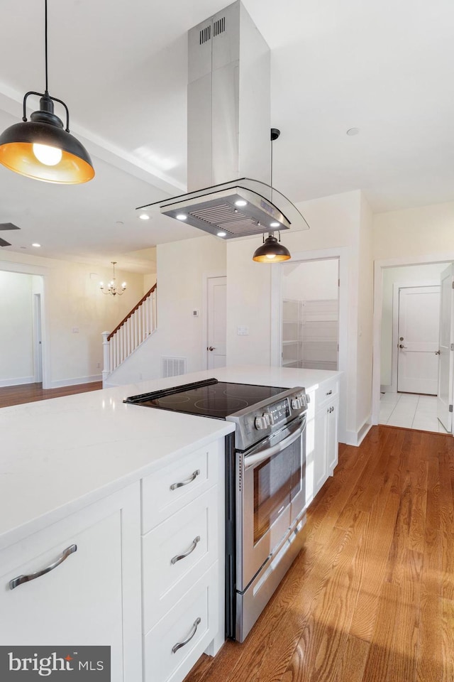 kitchen with decorative light fixtures, stainless steel electric range oven, light countertops, white cabinets, and island range hood