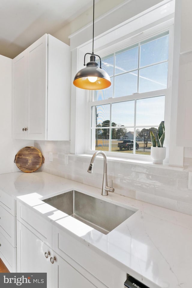 kitchen featuring light stone counters, decorative light fixtures, a sink, and white cabinetry