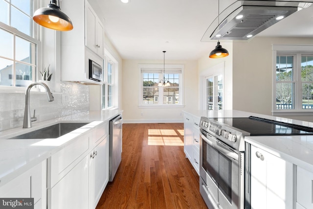 kitchen with appliances with stainless steel finishes, light stone countertops, white cabinetry, a sink, and exhaust hood