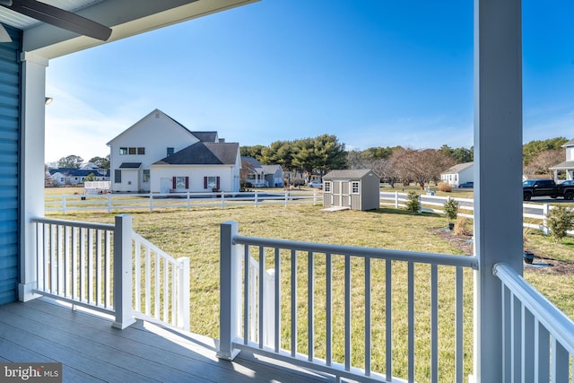 wooden terrace featuring a residential view, an outbuilding, fence, a yard, and a shed