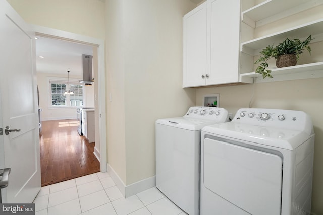 clothes washing area featuring washing machine and dryer, cabinet space, baseboards, and light tile patterned floors