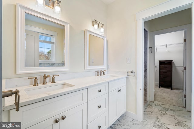 full bath featuring double vanity, marble finish floor, a spacious closet, and a sink