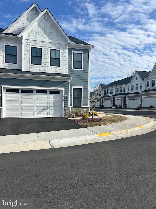 townhome / multi-family property with driveway, stone siding, and a garage