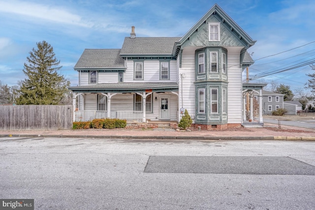 victorian-style house with roof with shingles, a porch, crawl space, and fence