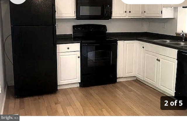 kitchen with dark countertops, black appliances, a sink, and light wood-style floors