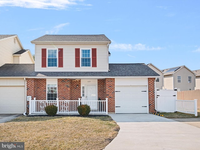 traditional-style house with brick siding, a porch, concrete driveway, an attached garage, and fence