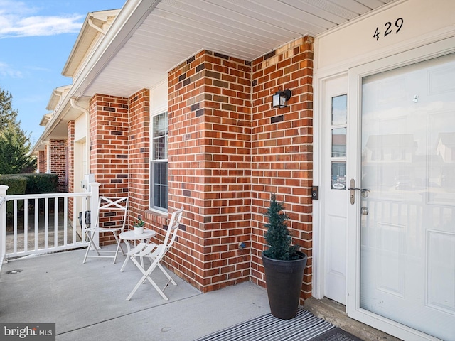 view of exterior entry featuring a porch and brick siding