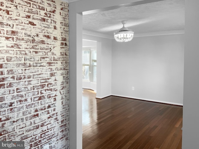 unfurnished room with a notable chandelier, ornamental molding, a textured ceiling, wood finished floors, and baseboards