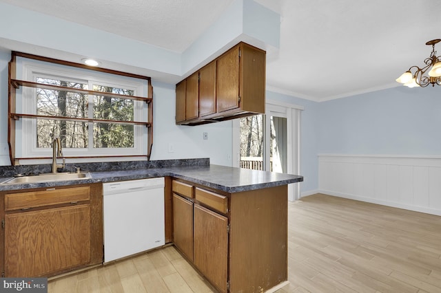 kitchen with dishwasher, light wood finished floors, dark countertops, and a sink