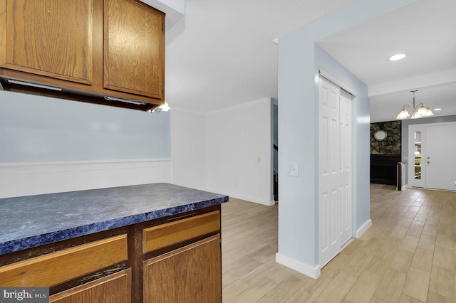 kitchen featuring wainscoting, brown cabinetry, dark countertops, and light wood-style floors