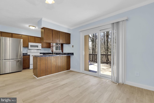 kitchen with a peninsula, white appliances, ornamental molding, light wood-type flooring, and dark countertops