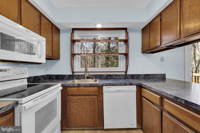 kitchen with white appliances, a sink, a healthy amount of sunlight, brown cabinetry, and dark countertops