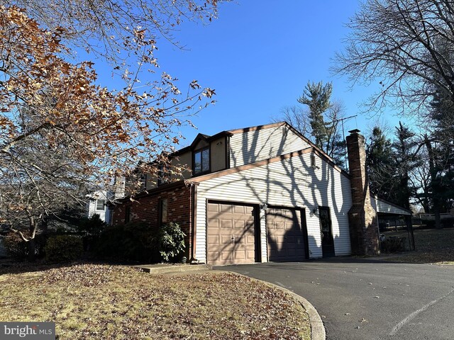 view of side of property featuring a garage, a chimney, aphalt driveway, and brick siding