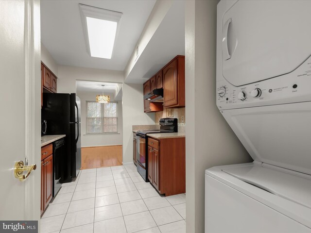 kitchen featuring stacked washer / dryer, under cabinet range hood, light countertops, black appliances, and light tile patterned flooring