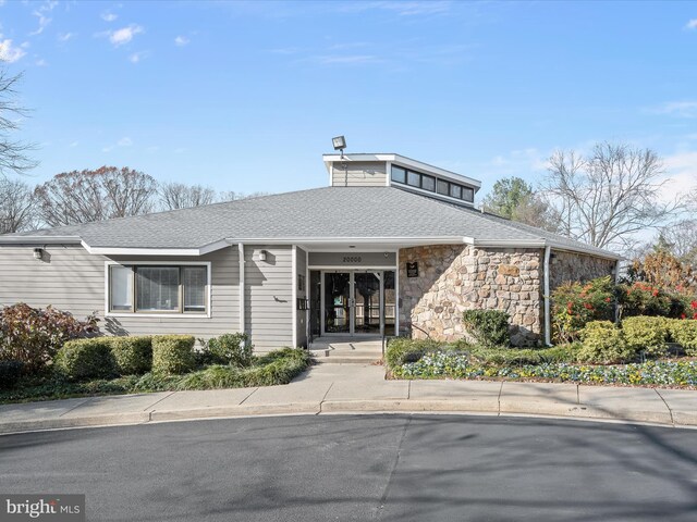 view of front of property featuring stone siding and roof with shingles