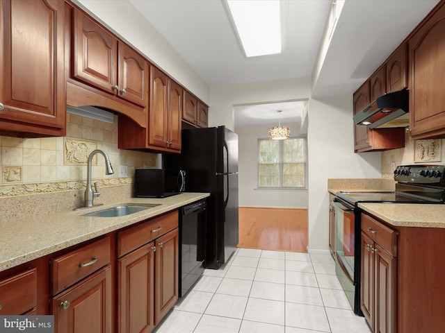 kitchen with light stone counters, decorative light fixtures, under cabinet range hood, black appliances, and a sink