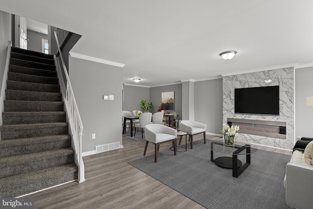 living area with visible vents, stairs, ornamental molding, a fireplace, and wood finished floors