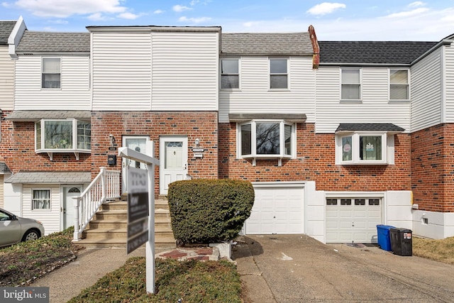 townhome / multi-family property with brick siding, a garage, driveway, and a shingled roof