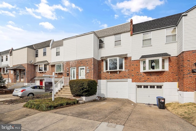 view of property with driveway, roof with shingles, an attached garage, a residential view, and brick siding